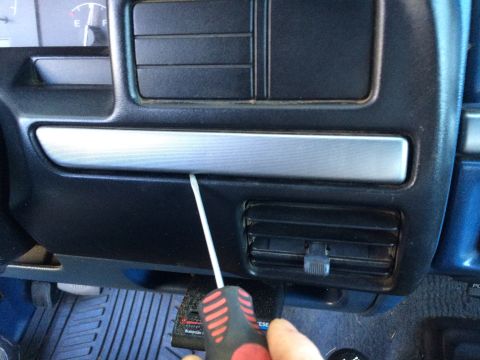 1990 Ford Bronco - A screwdriver is used to pry open a trim piece on the vehicle's dashboard near the air vents.