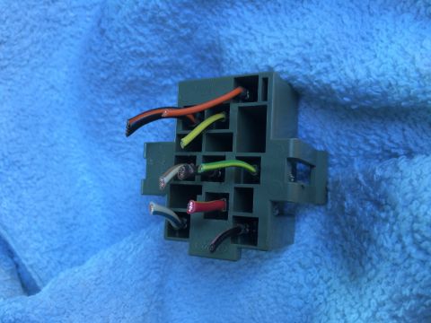 1990 Ford Bronco - A green plastic wiring harness connector with various colored wires is shown against a blue textured background.