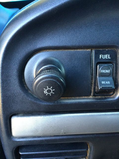 1990 Ford Bronco - Interior view of a vehicle's dashboard controls, including a headlight switch and fuel selection buttons.