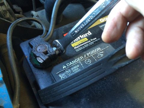 1990 Ford Bronco - A Craftsman wrench is used to tighten a corroded car battery terminal. The battery shows a 'Danger/Poison' warning.
