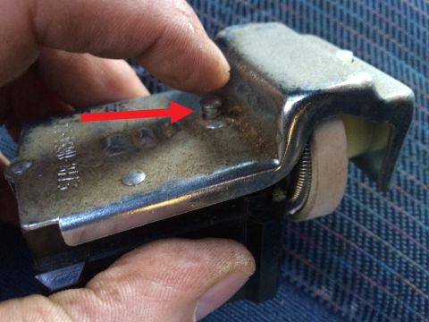 1990 Ford Bronco - A hand holds a headlight switch mechanism, with a red arrow indicating a specific screw on the metal housing.