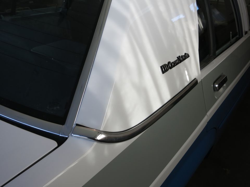 White car's rear pillar with a chrome trim piece and a black 'Crown Victoria' emblem
