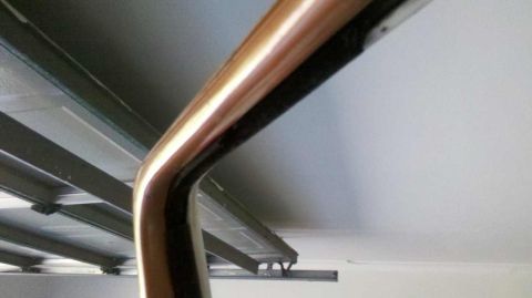 1982 Ford Bronco - A close-up of a curved chrome trim piece is visible against a white ceiling and metal support beams.