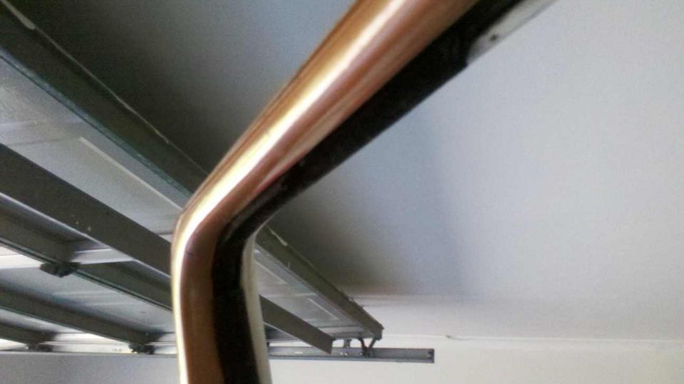 Curved chrome trim piece against a white ceiling and metal beams