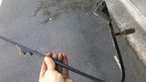 1982 Ford Bronco - A hand holds a metal rod with attached brackets, possibly a part from a vehicle.