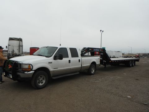 2000 Ford F-250 - A white pickup truck is hitched to a black gooseneck flatbed trailer in an outdoor lot.