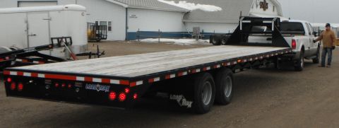 2000 Ford F-250 - A white Ford F-250 truck is connected to a long, flatbed trailer, with a man standing near the truck's cab.