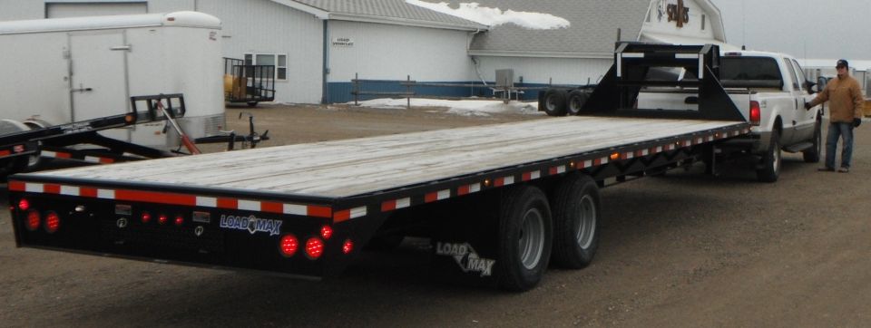 White Ford F-250 truck with a man standing by the driver's door, hitched to a large black flatbed trailer