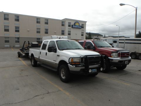 2000 Ford F-250 - A white 2000 Ford F-250 pickup truck is parked next to a red truck, towing a trailer.