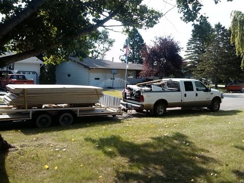 2000 Ford F-250 - A white 2000 Ford F-250 Super Duty pickup truck tows a trailer loaded with lumber down a residential street.