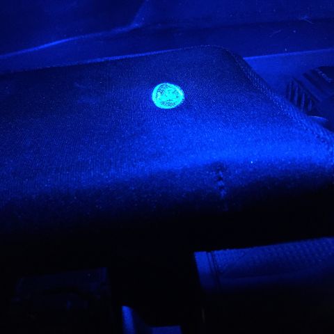 2007 Ford Crown Victoria - A circular mark glows under UV light on a dark interior car surface.