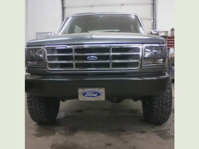 Front view of a lifted dark gray Ford Bronco with chrome grille and off-road tires in a garage