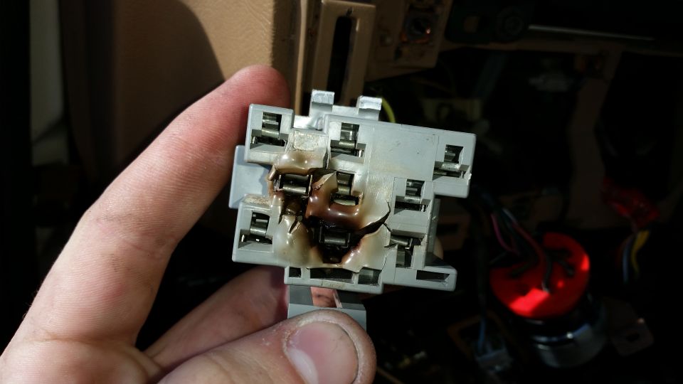 Hand holding burnt melted electrical connector socket from dashboard