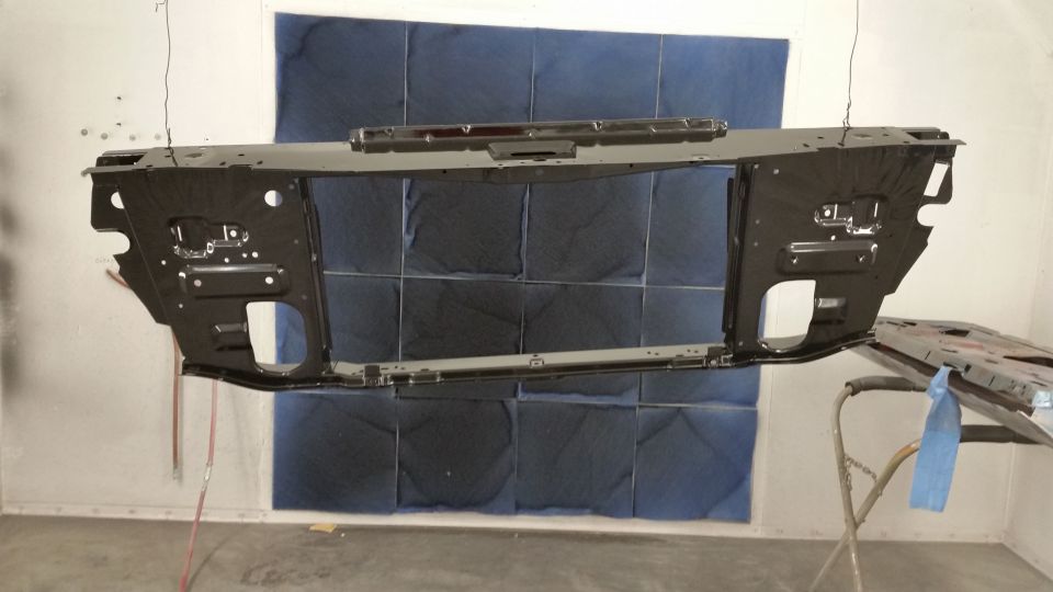 Black metal car front subframe hanging in a spray booth, viewed ...