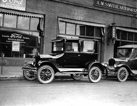 1909 Ford Model T - Two vintage Ford vehicles are parked in front of a dealership with visible signage.