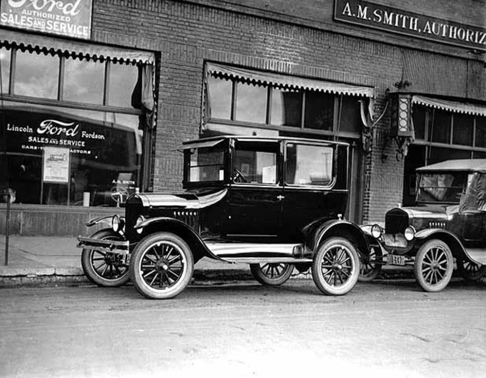 Black sedan and touring car parked outside a brick building with awnings
