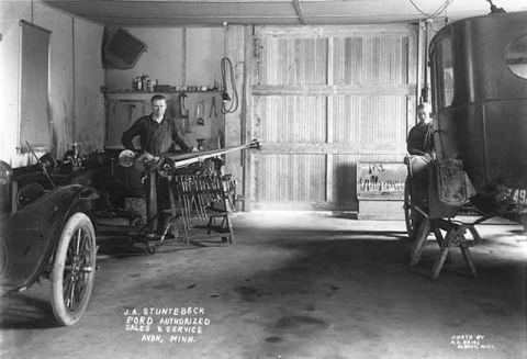 1909 Ford Model T - A man stands by a 1909 Ford Model T in a dealership garage, with a horse-drawn carriage also visible.