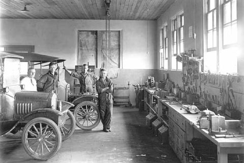 1909 Ford Model T - Four men stand with two Ford Model T vehicles inside a workshop, likely a dealership or factory.
