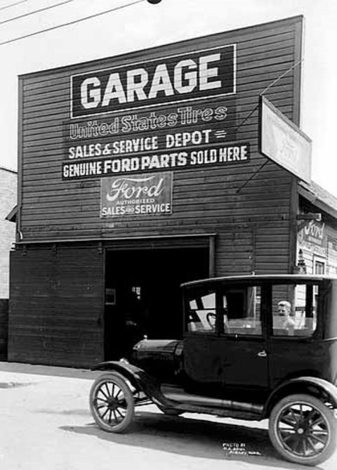 1909 Ford Model T - A 1909 Ford Model T sits outside a garage that clearly states 'Genuine Ford Parts Sold Here'.
