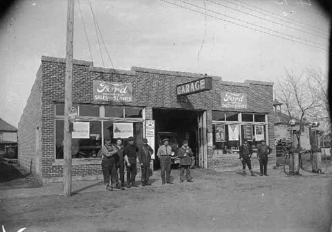 1909 Ford Model T - Men stand outside a brick Ford dealership and garage, with visible "Ford Sales & Service" signage.