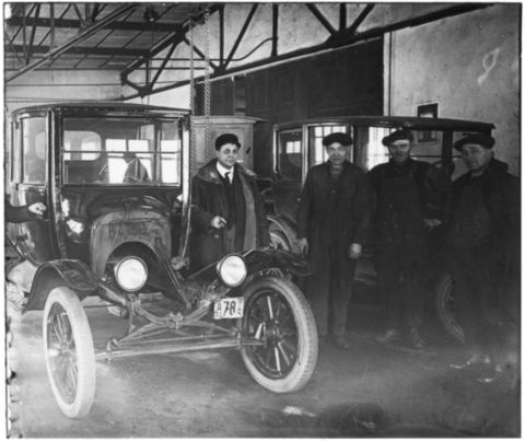 1909 Ford Model T - A group of men stand with a 1909 Ford Model T inside a garage, possibly a dealership or factory.