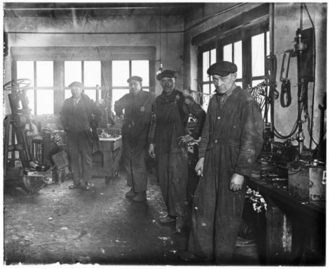 1909 Ford Model T - Workers stand in a busy workshop filled with equipment and tools.