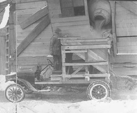 1909 Ford Model T - A 1909 Ford Model T truck is being loaded with grain from a wooden structure.