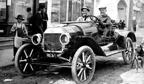 1909 Ford Model T - Two men enjoy a ride in a 1909 Ford Model T speedster on a street with a young boy watching.