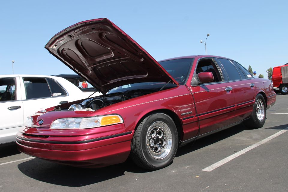 Red Ford Crown Victoria with hood open, showing engine modifications. Custom wheels are visible