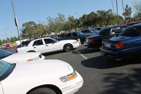 2004 Ford Crown Victoria - A collection of Ford Crown Victorias, including white, black, and blue models, are parked together in a lot.