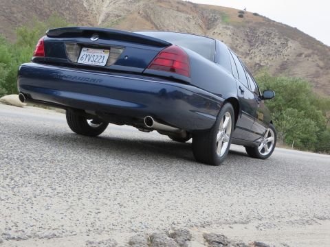 2003 Mercury Marauder - Rear view of a dark blue 2003 Mercury Marauder sedan driving on a road with hills in the background.
