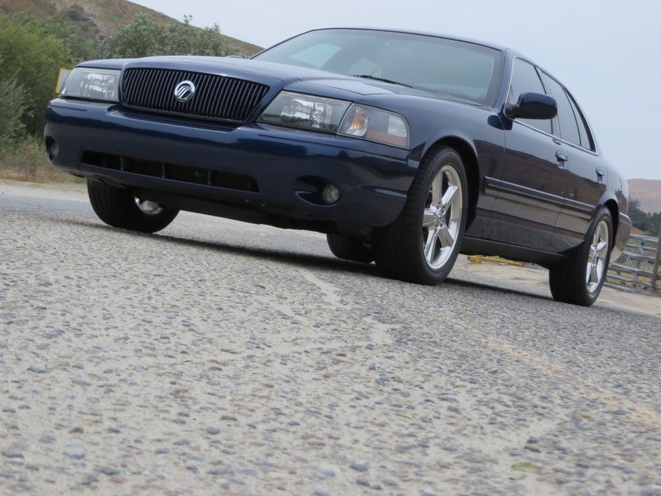 Dark blue sedan parked on a road. The front grille and headlights are visible