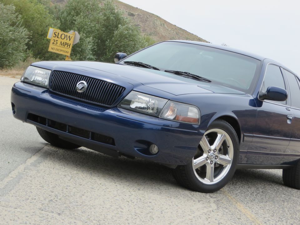 Blue 2003 Mercury Marauder front quarter view with chrome wheels and a "SLOW 25 MPH" sign in the background