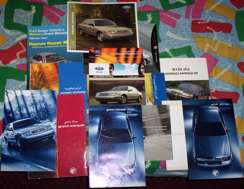 1999 Mercury Grand Marquis - Various brochures for Mercury Grand Marquis and Ford Crown Victoria vehicles are spread out on a colorful patterned surface.
