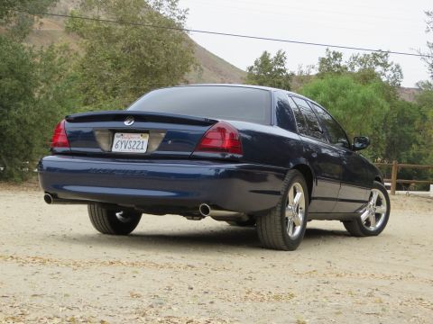 2003 Mercury Marauder - Rear view of a dark blue 2003 Mercury Marauder parked on a dirt road with trees in the background.
