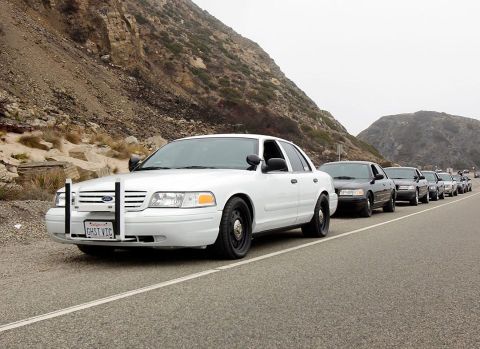 2004 Ford Crown Victoria - A convoy of Ford Crown Victoria sedans, some white and some dark, are lined up along a roadside with a steep, rocky hill. The lead vehicle…