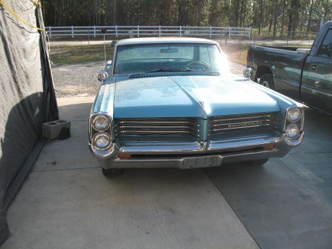 1972 Ford Ranchero - Front view of a blue 1963 Pontiac Bonneville, a prominent chrome grille and stacked headlights, parked next to a pickup truck.