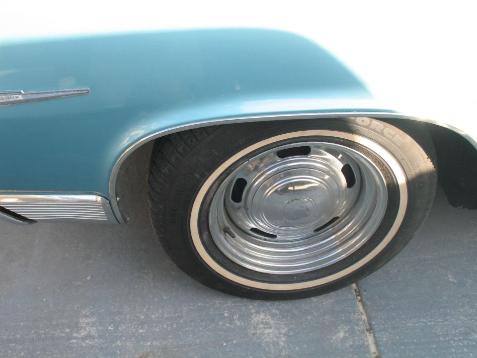 Close-up of a car's rear wheel with a whitewall tire and chrome hubcap. Blue fender above