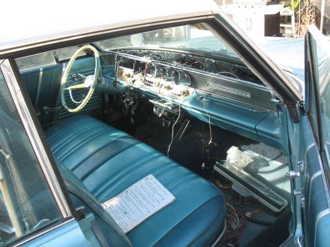 1972 Ford Ranchero - The interior of a classic car features teal seats and a dashboard with exposed wiring, along with a notebook on the passenger seat.