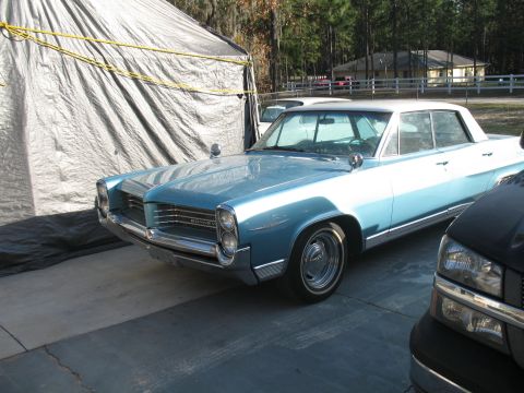 1972 Ford Ranchero - A 1963 Pontiac Bonneville is parked next to a black pickup truck under a tarp.