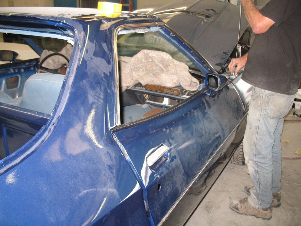 Car door and interior of a blue vehicle being worked on, with a person in the background