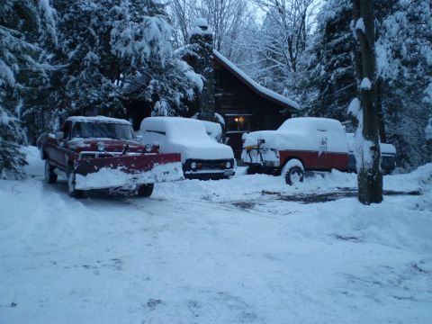 1979 Ford Bronco - Multiple trucks are parked in the snow outside a cabin, with one truck equipped with a snow plow.