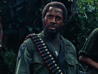 2000 Mercury Grand Marquis - A man in a military uniform wears an ammunition belt across his chest, with foliage in the background.