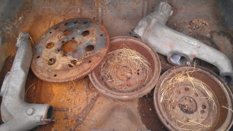 1970 Pontiac Trans Am - Assorted rusty car parts including a flywheel, brake drums, and exhaust manifold are piled together.