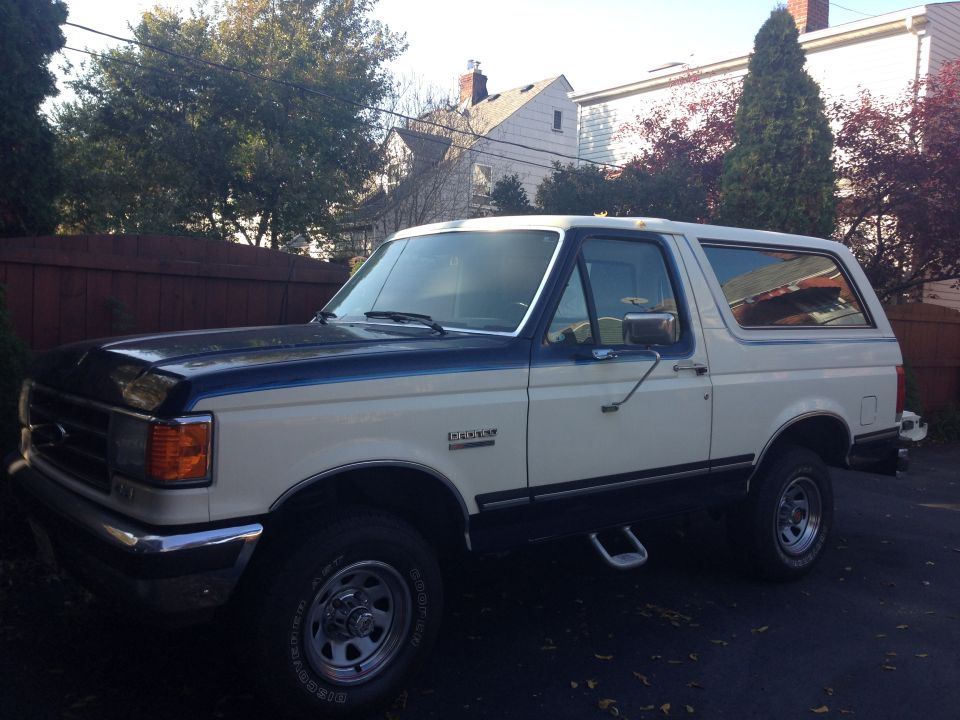 White and dark blue Ford Bronco SUV parked in driveway, driver-side front three-quarter view
