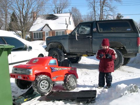 1986 Ford Bronco - A child stands next to a Ford Bronco and a toy truck in a snowy yard.