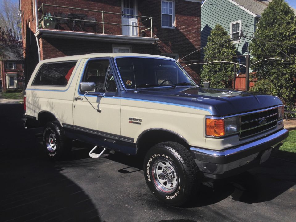 Tan and blue Ford Bronco SUV, 3/4 front passenger view, parked on driveway by brick house