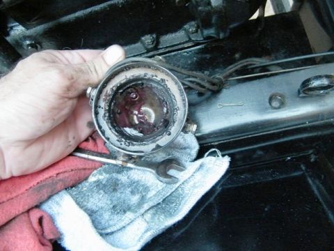 1915 Ford Model T - Disassembled greasy automotive part being held by a hand, with tools and rags nearby.