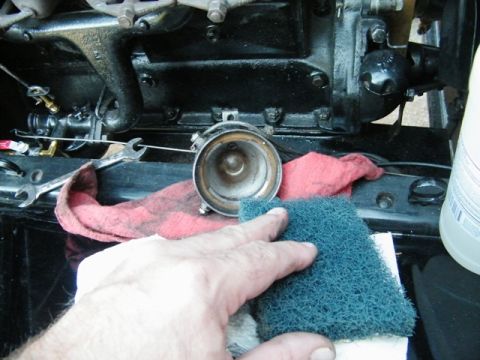 1915 Ford Model T - A hand is cleaning a metal component of a vehicle's engine with a scrub pad and rags nearby.