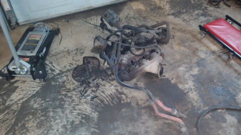 1995 Ford Bronco - Engine assembly components are laid out on a concrete floor, accompanied by a floor jack and a red creeper.